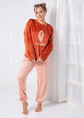 Woman wearing a rust-colored sweatshirt with 'Feathers' logo and pink patterned pants against a white curtain background.